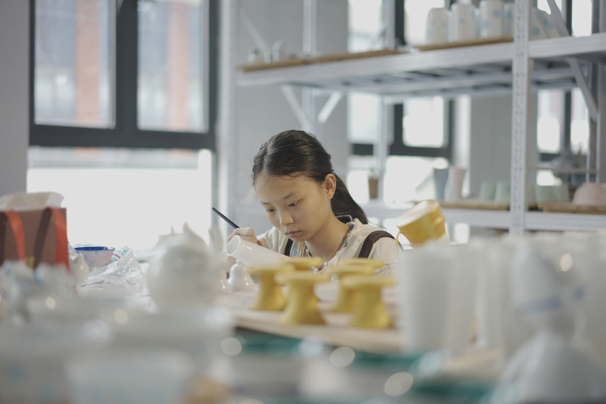 Company photograph of a person at a workbench with a brush, vessels and tools