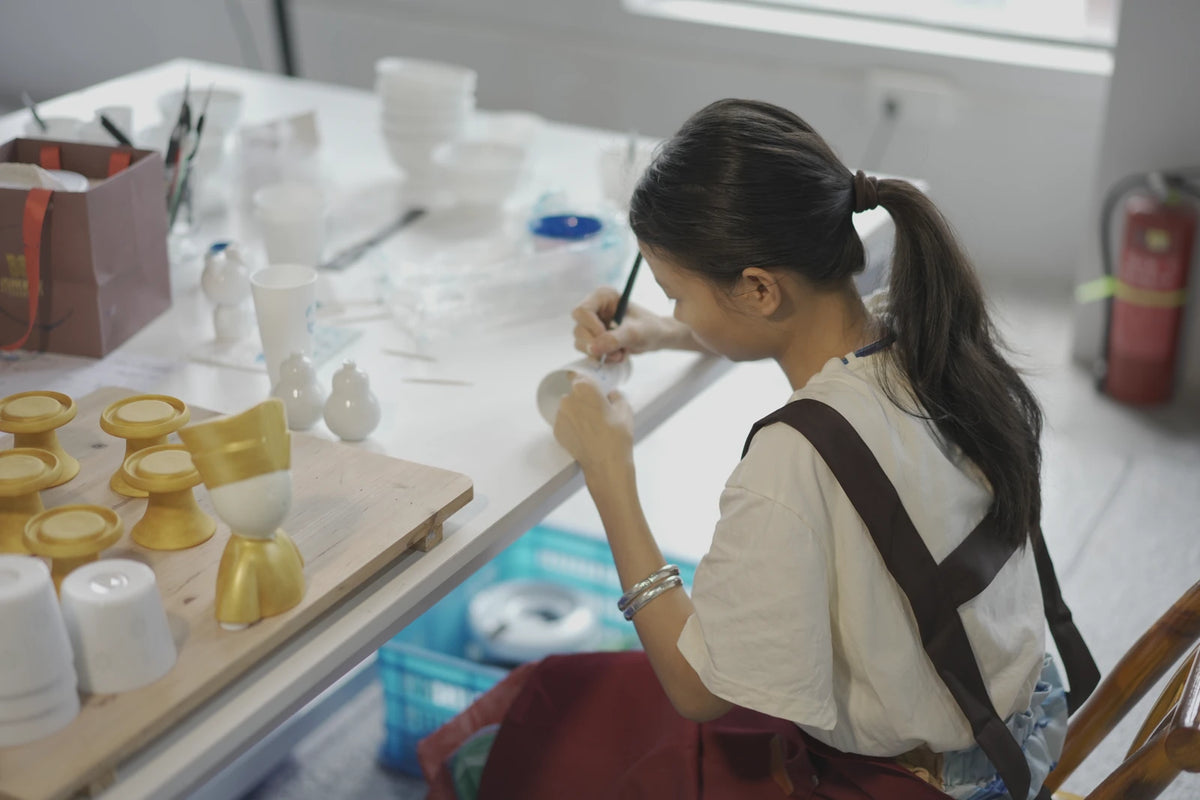 Company workshop photograph of hands working on white porcelain at a workbench