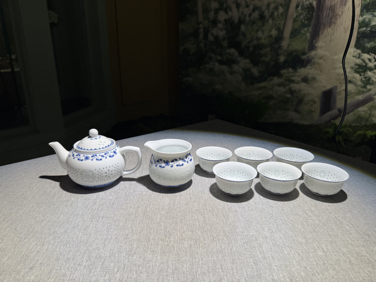 Actual blue-and-white Blossom Vine Linglong teapot, pitcher and cups together on a fabric-covered table