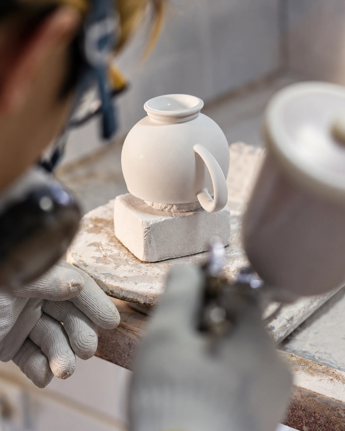 Company workshop photograph, edited: porcelain cup, protected hand and tool at the original workstation.