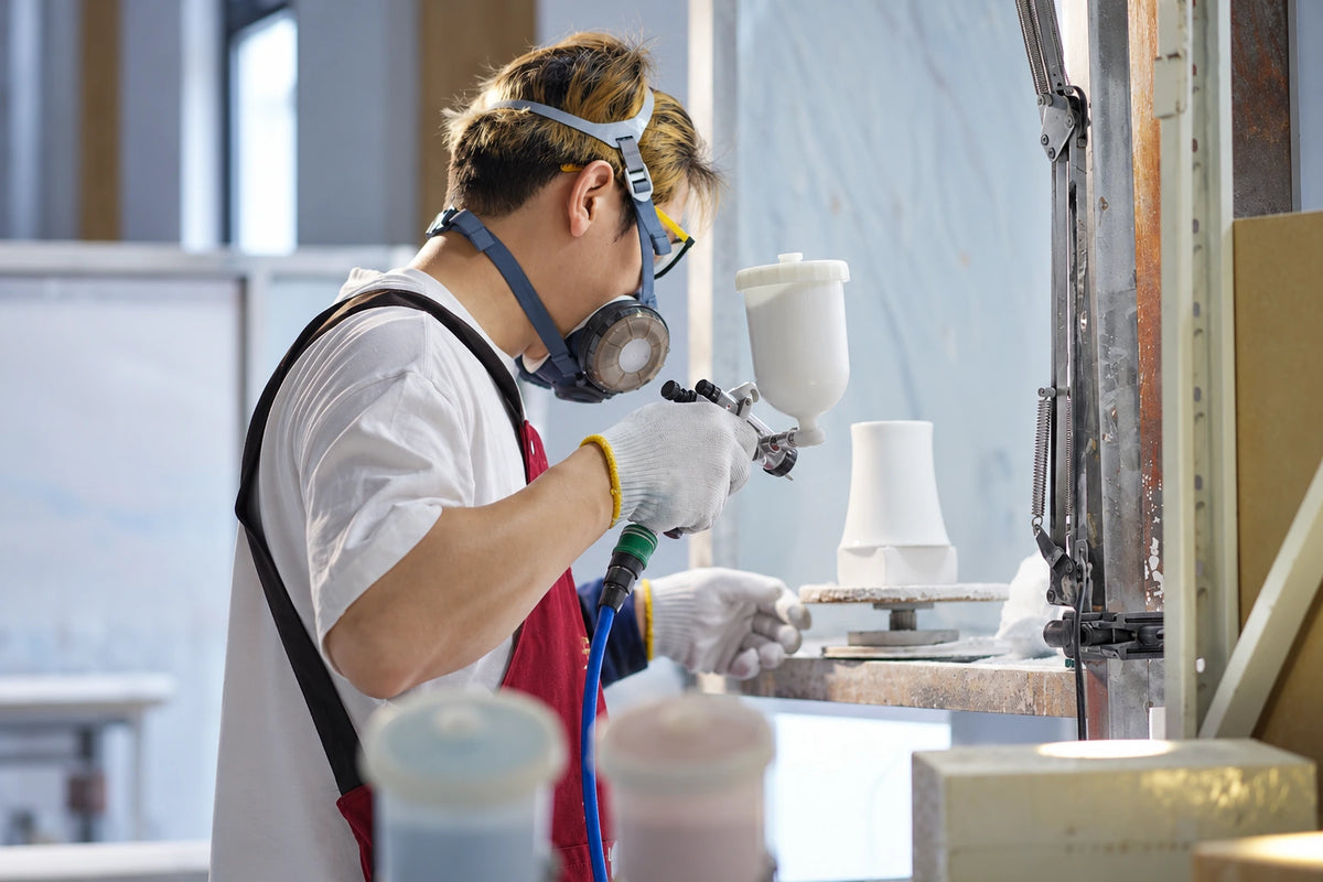 Company workshop photograph, edited: an operator with goggles and respirator using a spray tool.